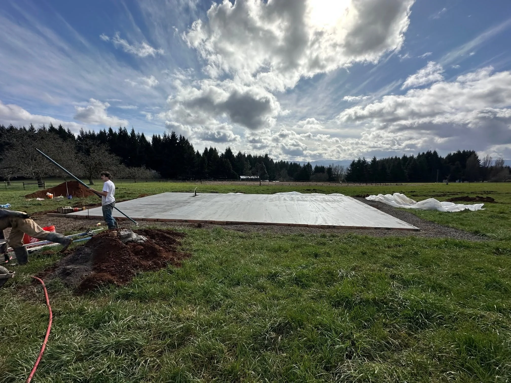 Excavated residential lot with white geotextile fabric and stockpiled soil on rural property