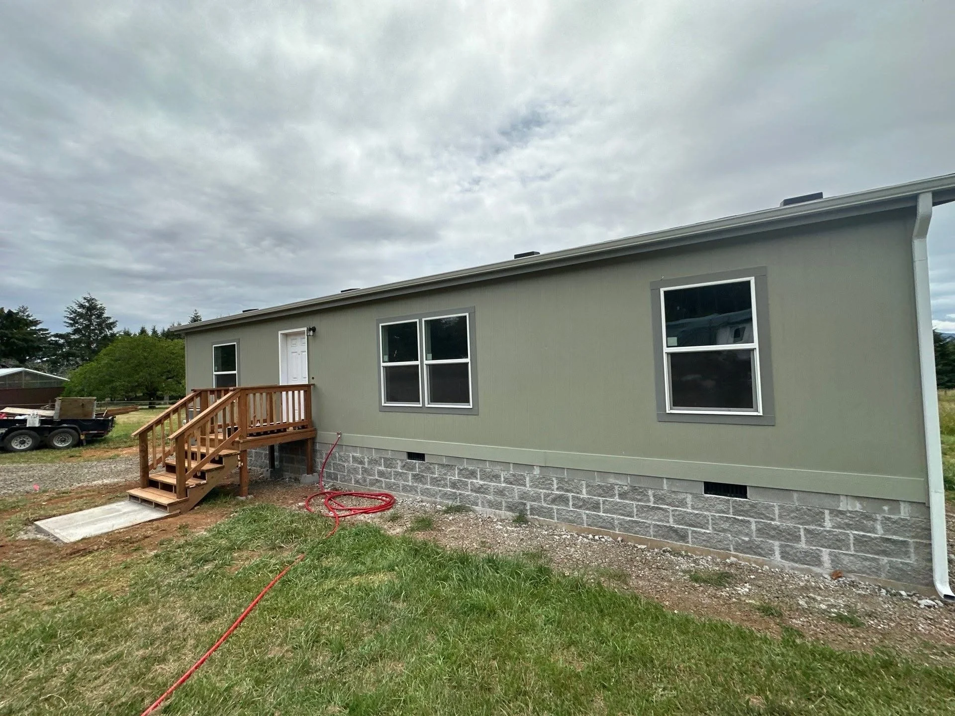 Mobile home with green siding, concrete block foundation, wooden deck, and white windows
