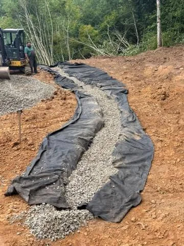 Curved drainage trench with landscape fabric and crushed stone on sloped earthwork