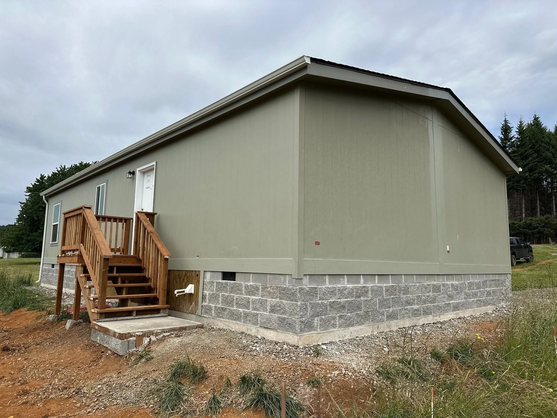 Manufactured home with stone foundation, wooden entry deck, and gravel site preparation