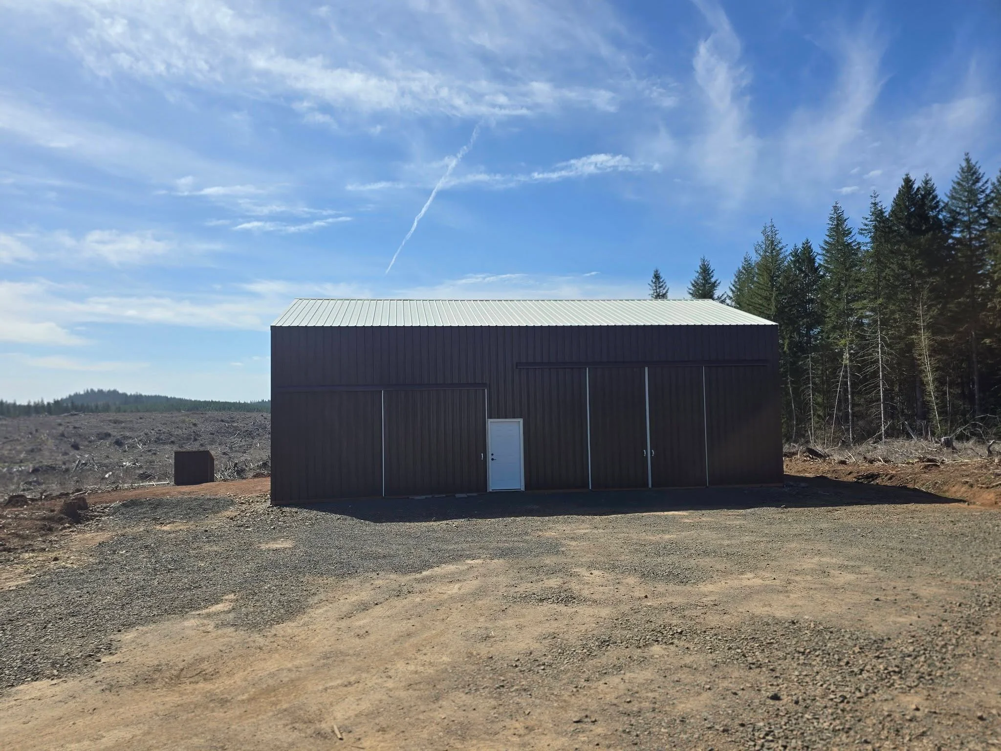 Black corrugated metal building with standing seam roof and bay doors on gravel site