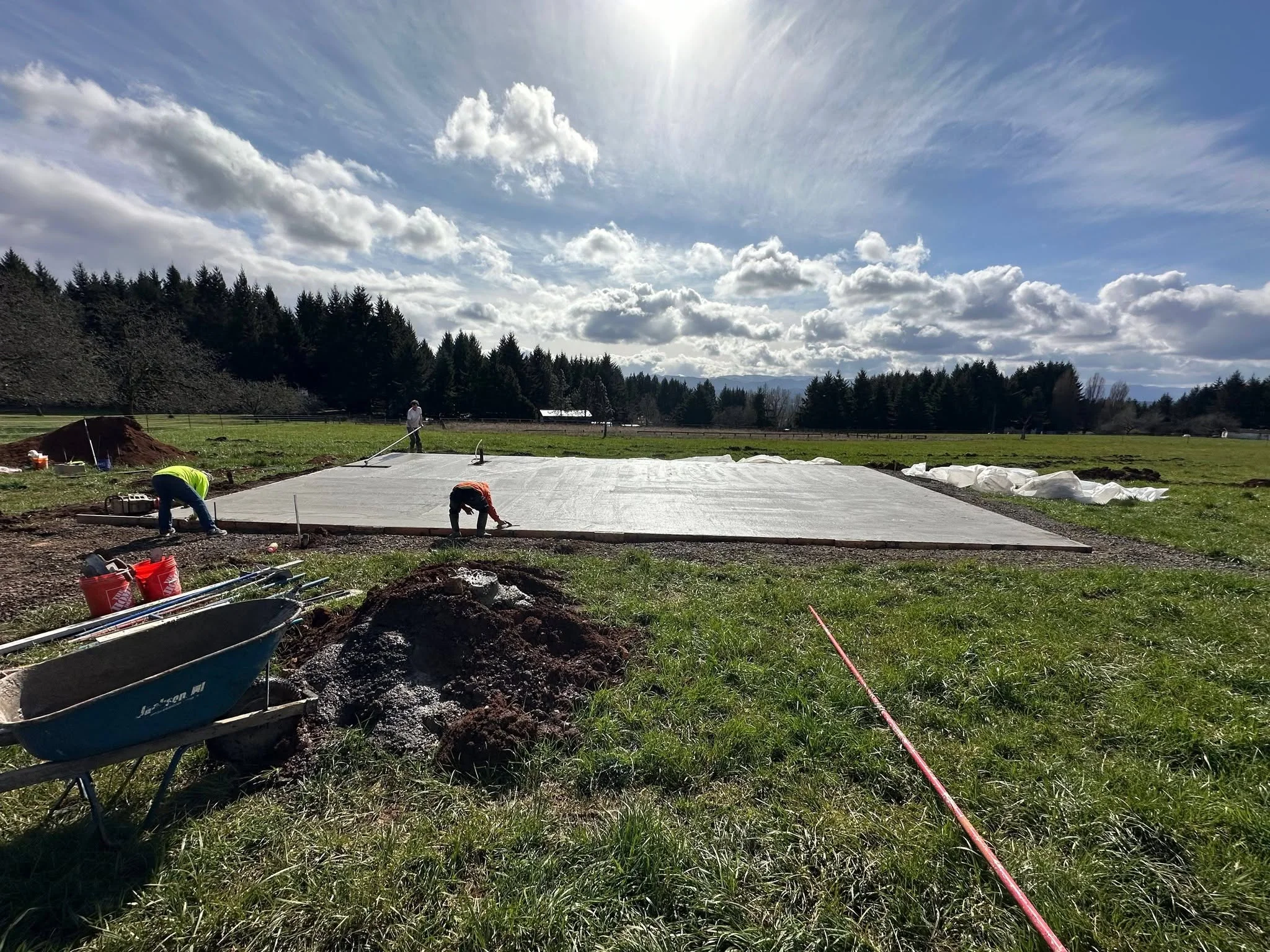 Foundation pad preparation with excavated soil, compacted base, and landscape fabric on rural property