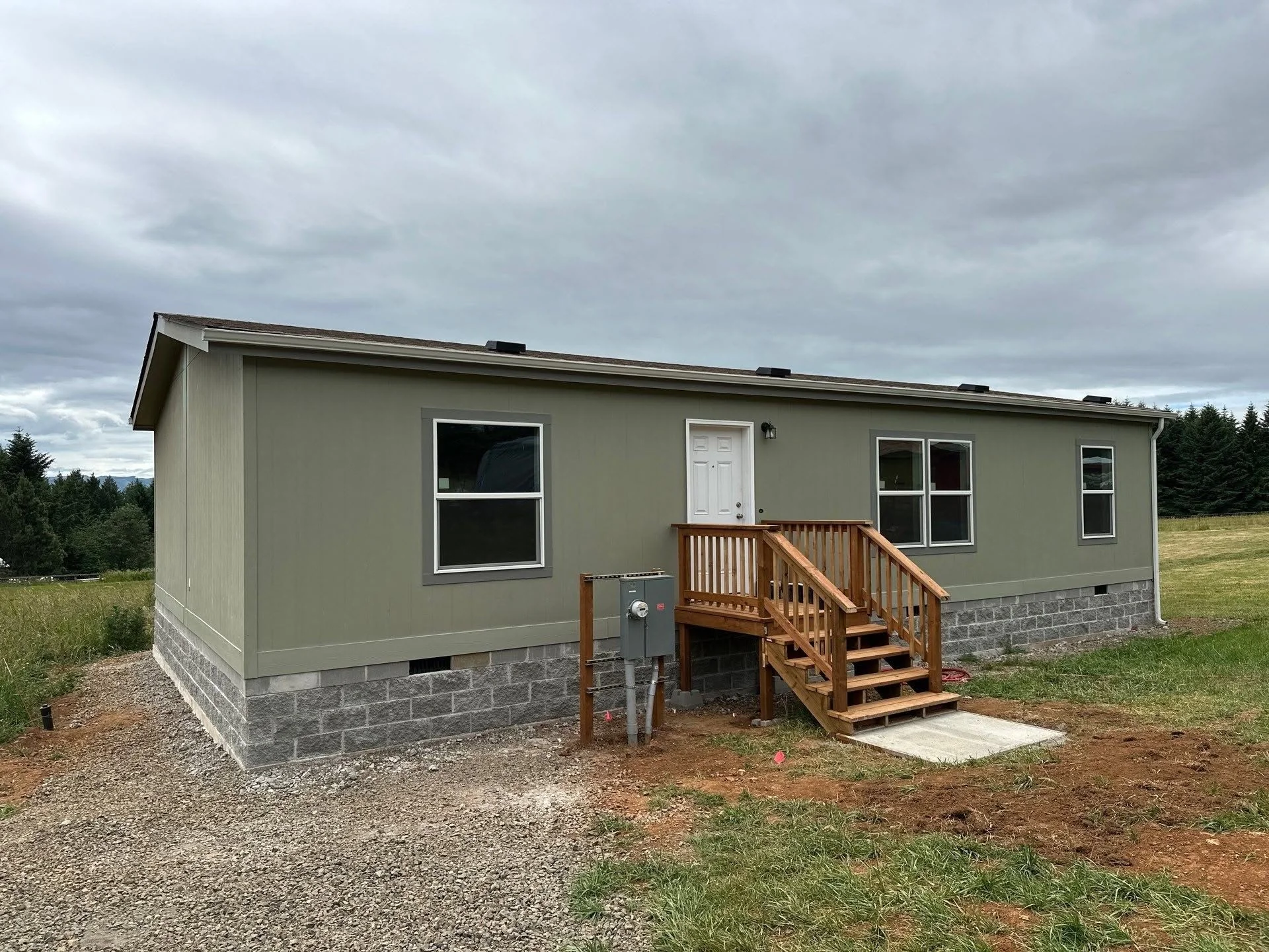 Mobile home on concrete block foundation with wooden deck stairs and white trim windows