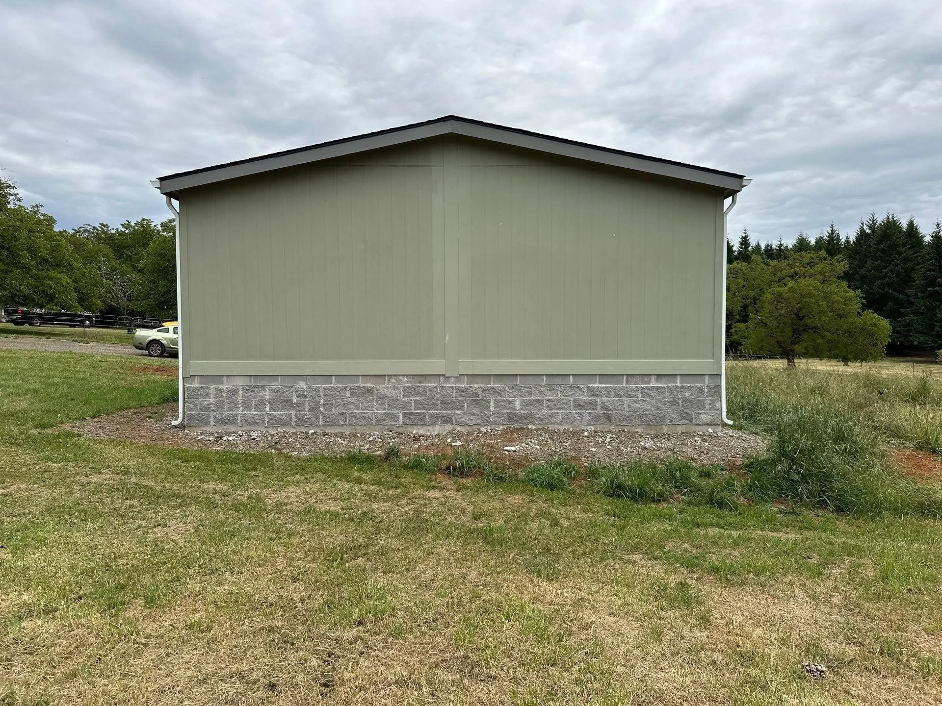Mobile home with stone veneer foundation skirt and metal guttering system on prepared gravel base