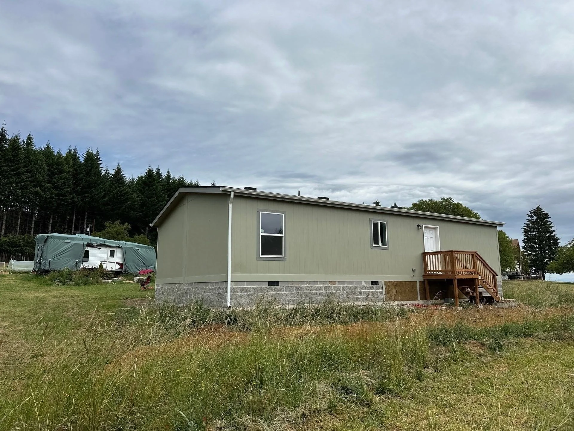 Mobile home with concrete block foundation, stone veneer skirt, and wooden deck installation