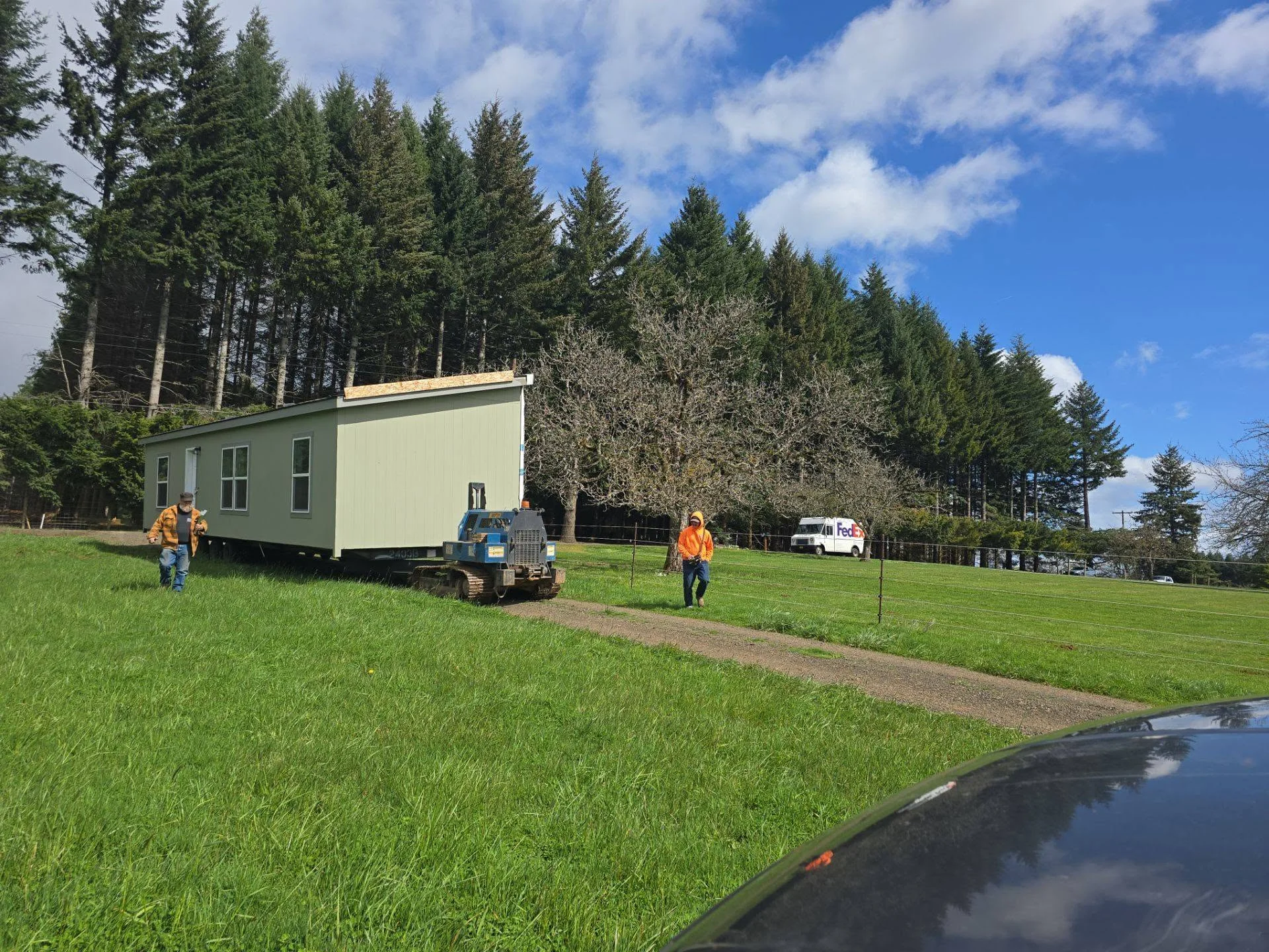 Mobile home with sage green siding being positioned on prepared lot with heavy equipment and crew