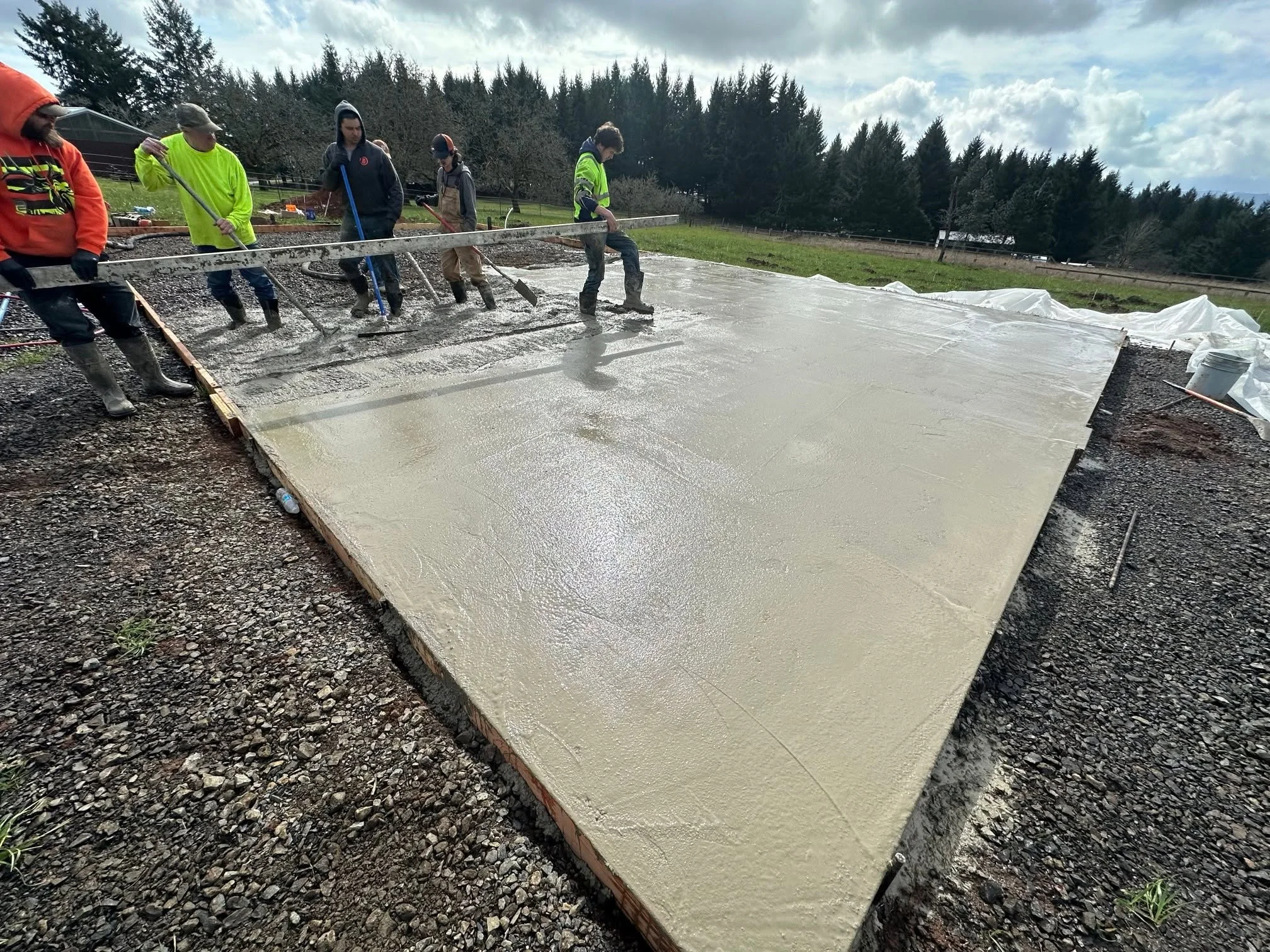 Crew finishing fresh concrete foundation pour with wooden forms and screeding tools